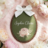Embroidered oval nursery hoop sign with dark green fabric, white bow, Sophia Claire and peony